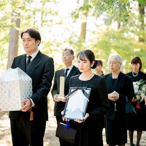 家族が故人様の遺影と遺骨を抱えて歩いている場面