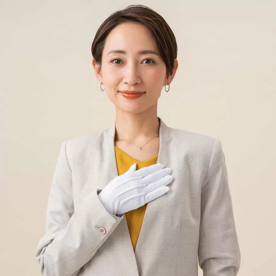 白い手袋をしたスーツの女性が右手を左胸に当てている